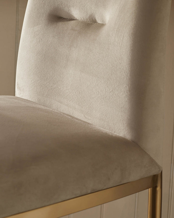 Close-up of a stylish chair with a plush, neutral-toned cushion and sleek gold metal frame.