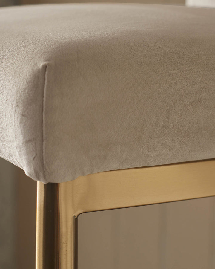 Close-up of a stylish chair seat with plush neutral fabric and a sleek, gold-finish metal frame. Modern design.