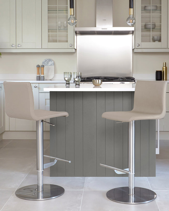 Two stylish bar stools with neutral upholstery and silver metal bases are positioned in front of a kitchen island.
