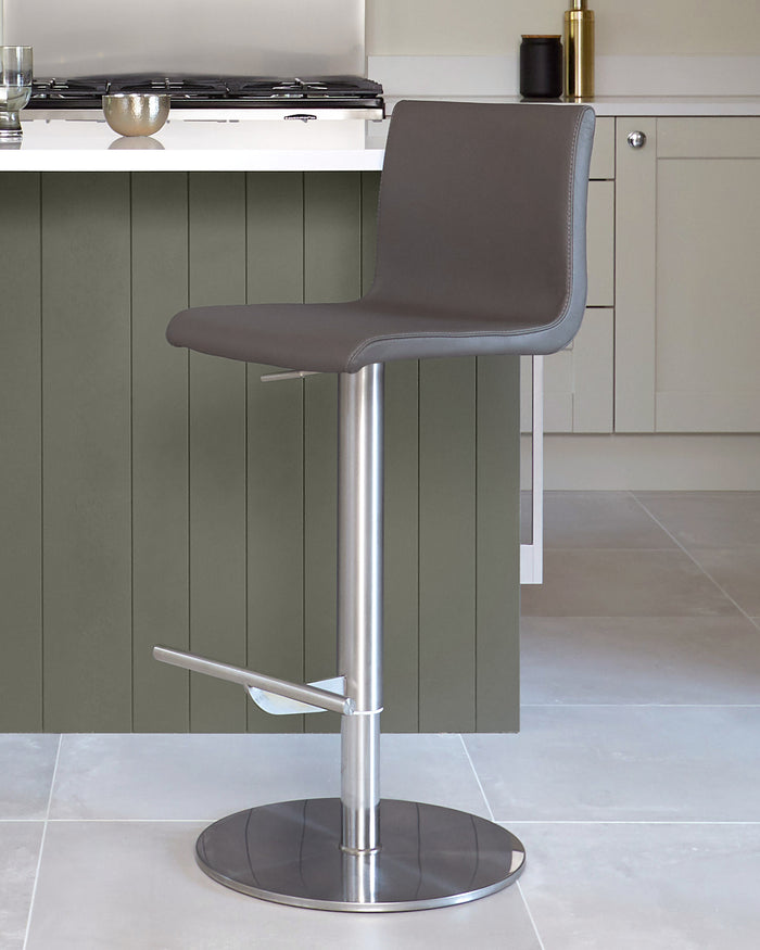A grey bar stool sits in front of a kitchen island, featuring a sleek metal base and footrest.