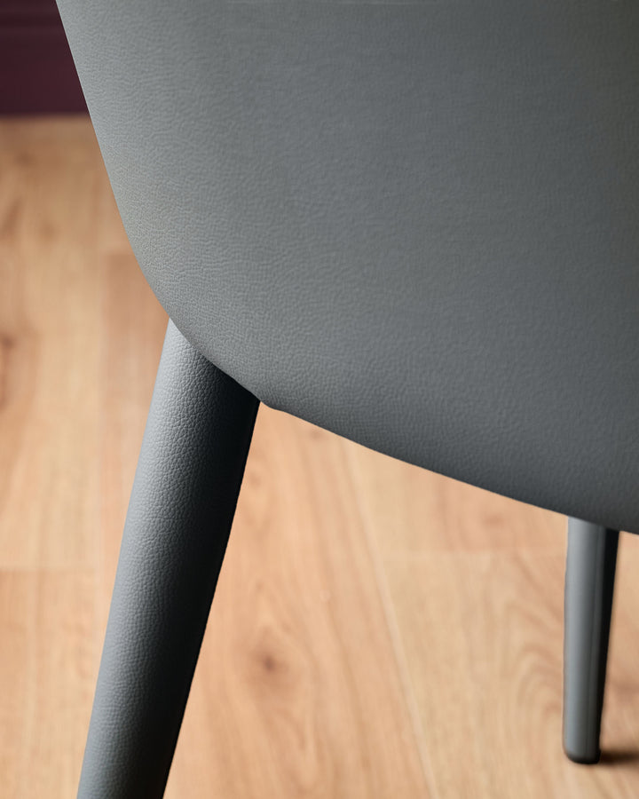 Dark grey faux leather dining chair with black legs, shown at an angle on a wooden floor.