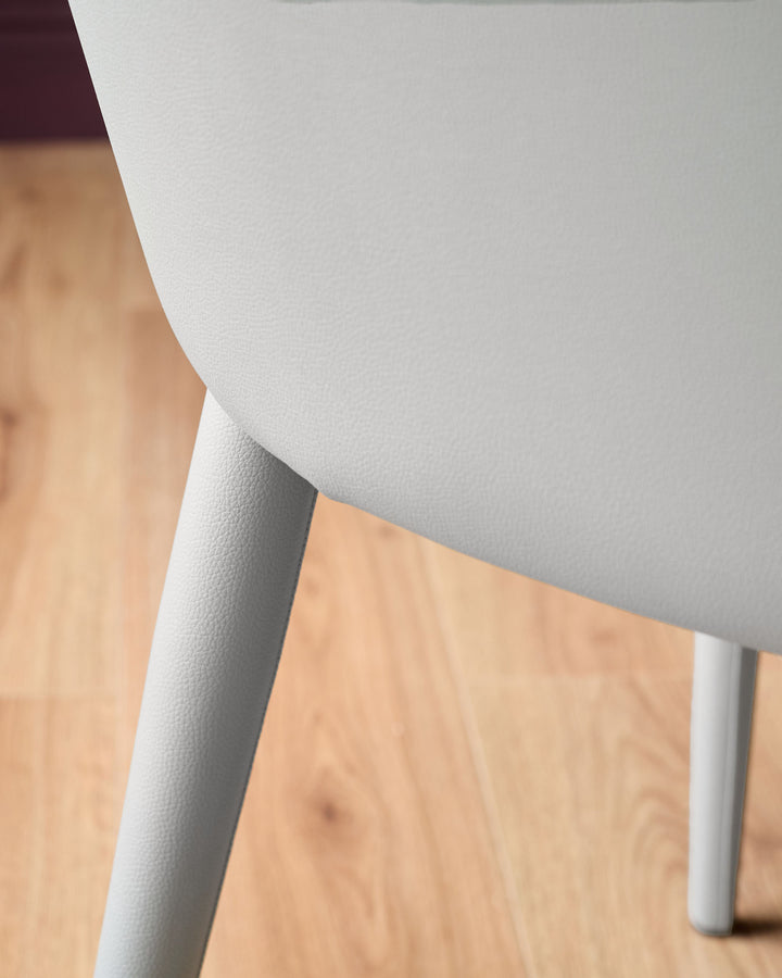 Kyro faux-leather dining chair in light grey, angled side view showing curved backrest and white leg detail on wooden floor.