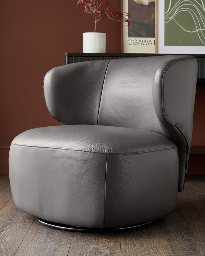 A stylish, grey leather swivel chair on a wooden floor, in front of a brown wall and dark wood cabinet.