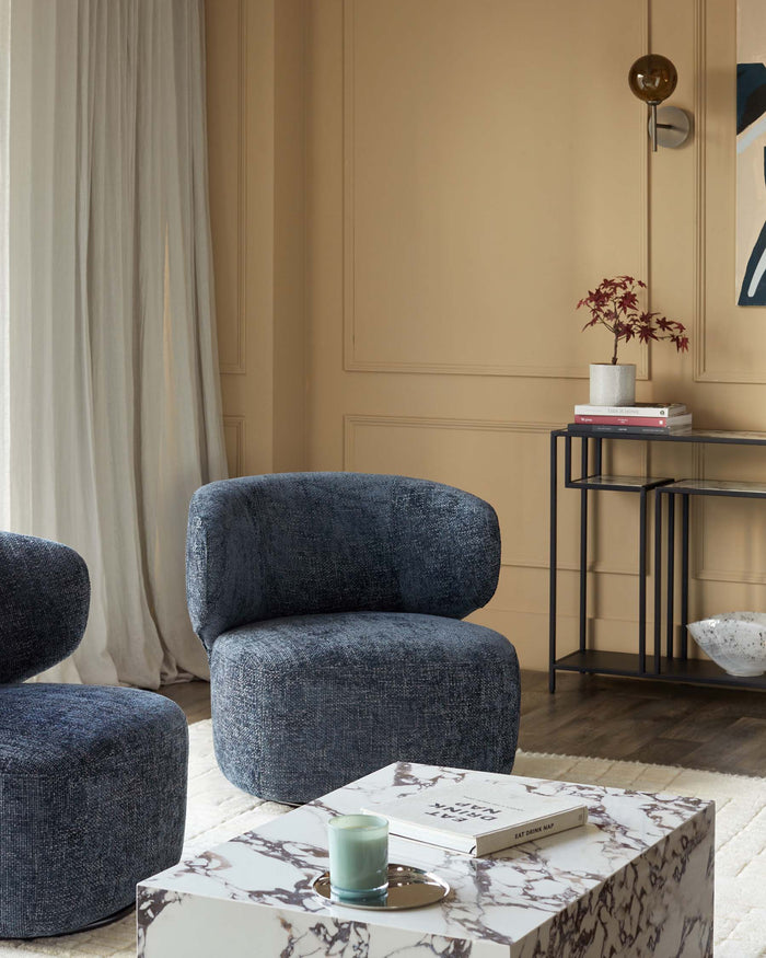 Stylish living room featuring two blue upholstered armchairs, a marble coffee table, and a black console table.