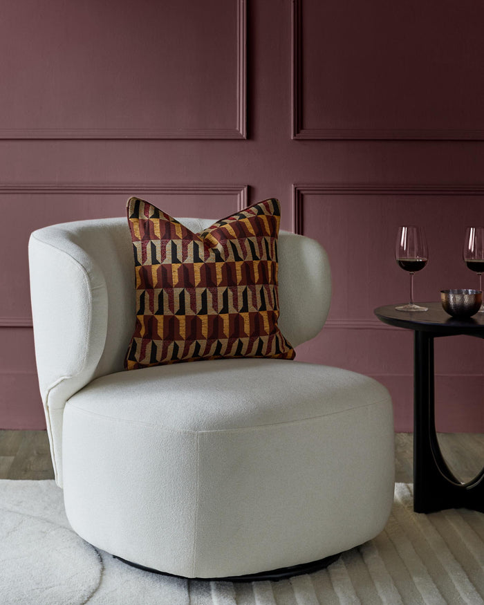 A cream swivel chair with patterned cushion, a black side table and two glasses of red wine against a panelled wall.