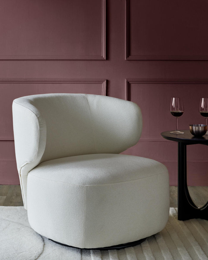 A stylish white swivel chair sits beside a dark side table with wine glasses, against a deep pink panelled wall.