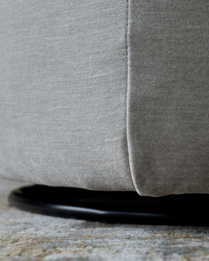 Close-up of a grey, upholstered furniture piece with a black base, sitting on a textured rug. Modern design.