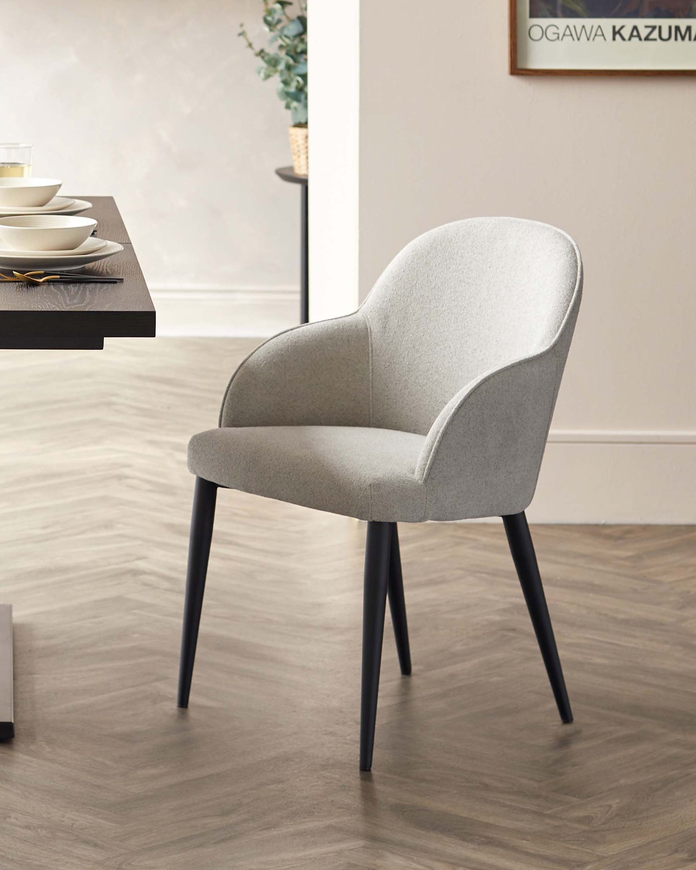 Modern light grey upholstered dining chair with a curved back and seat design, featuring dark tapered wooden legs.