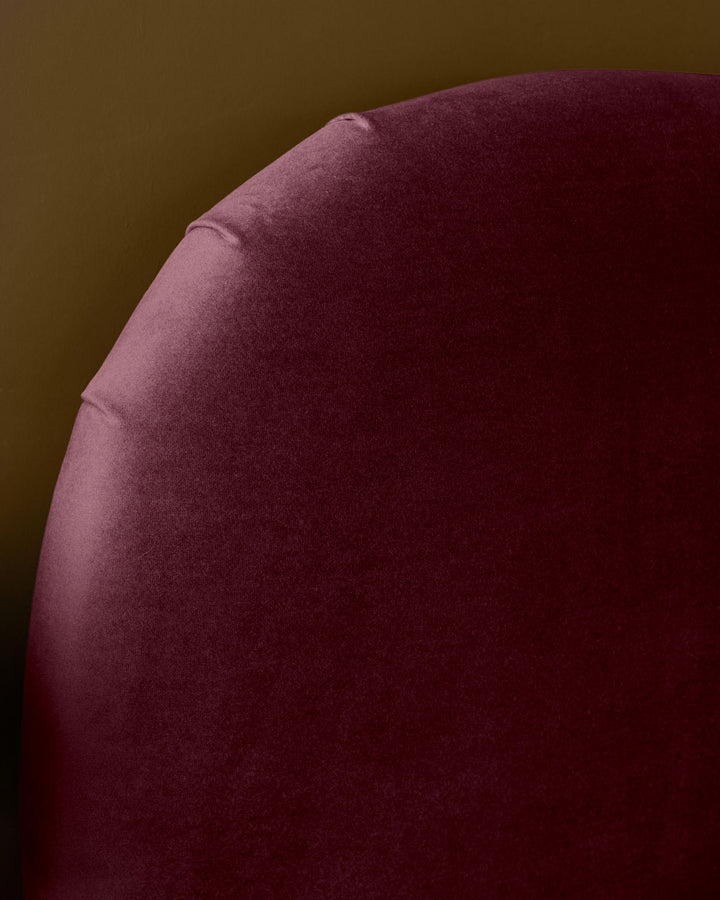 Plum velvet ottoman bed with curved rounded edges, shown at side angle against neutral background.