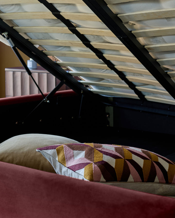Plum velvet ottoman bed with open storage, geometric patterned cushion, natural wood slatted base visible from above.