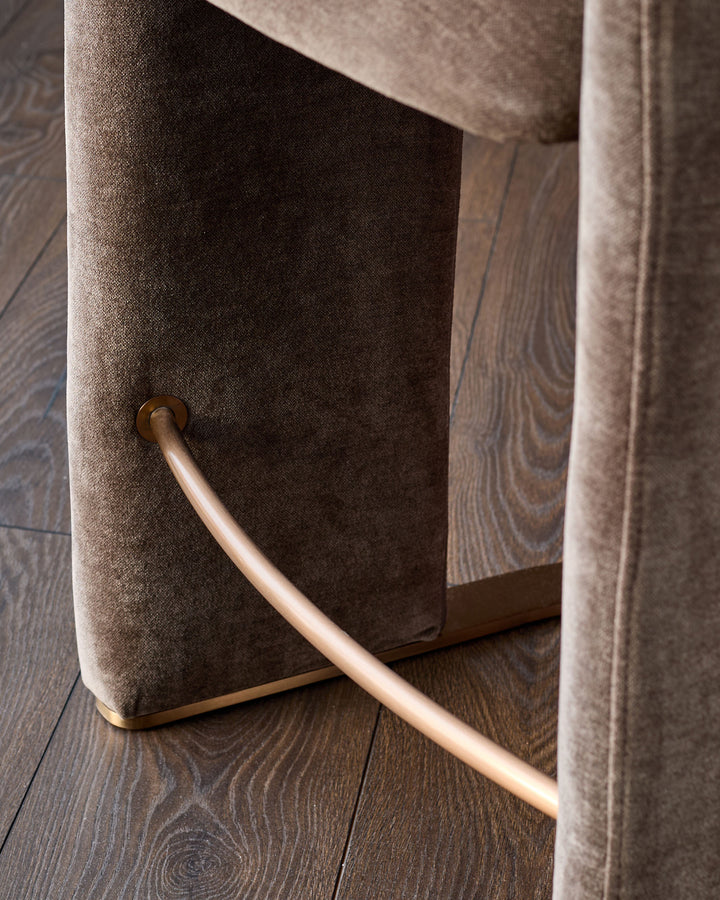 Leighton bar stool detail showing brushed bronze handle against mocha fabric upholstery on dark wood flooring.