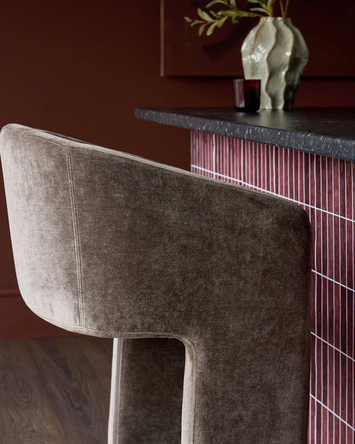 Leighton brushed bronze cantilever bar stool in mocha fabric, side view showing curved backrest and metal frame detail.