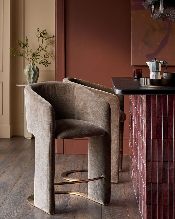 Leighton brushed bronze cantilever bar stool in mocha fabric, shown in a kitchen setting with footrest detail visible.