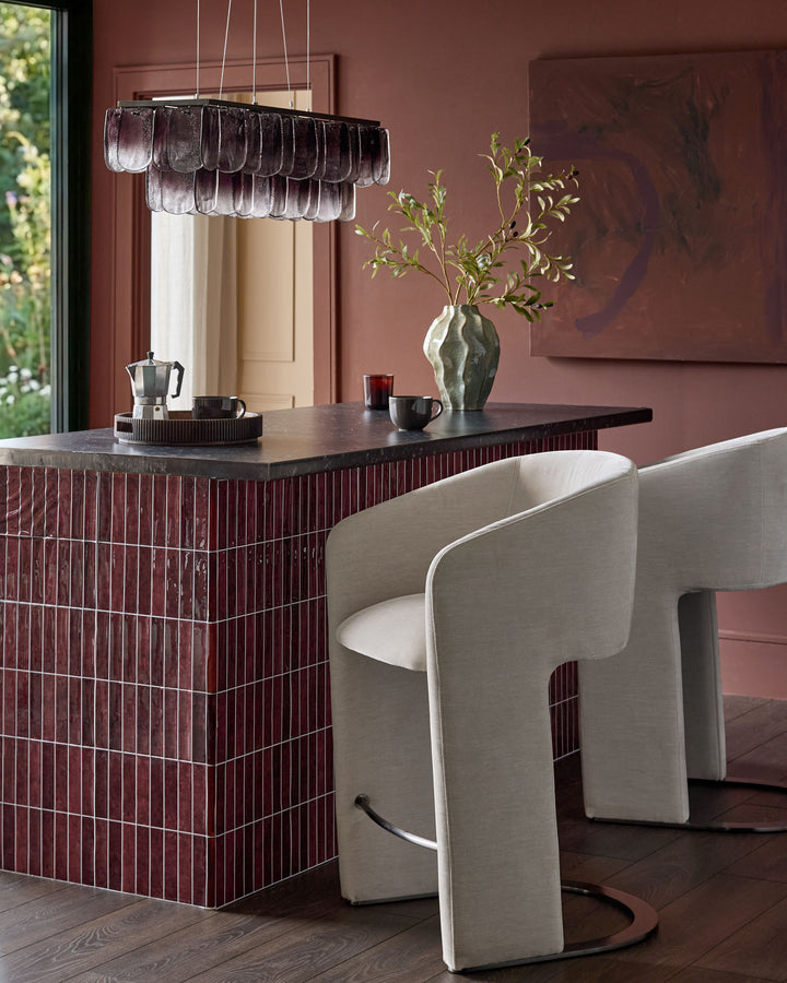 Leighton black steel cantilever bar stool in natural grey fabric, shown at burgundy kitchen island with modern curved backrest.
