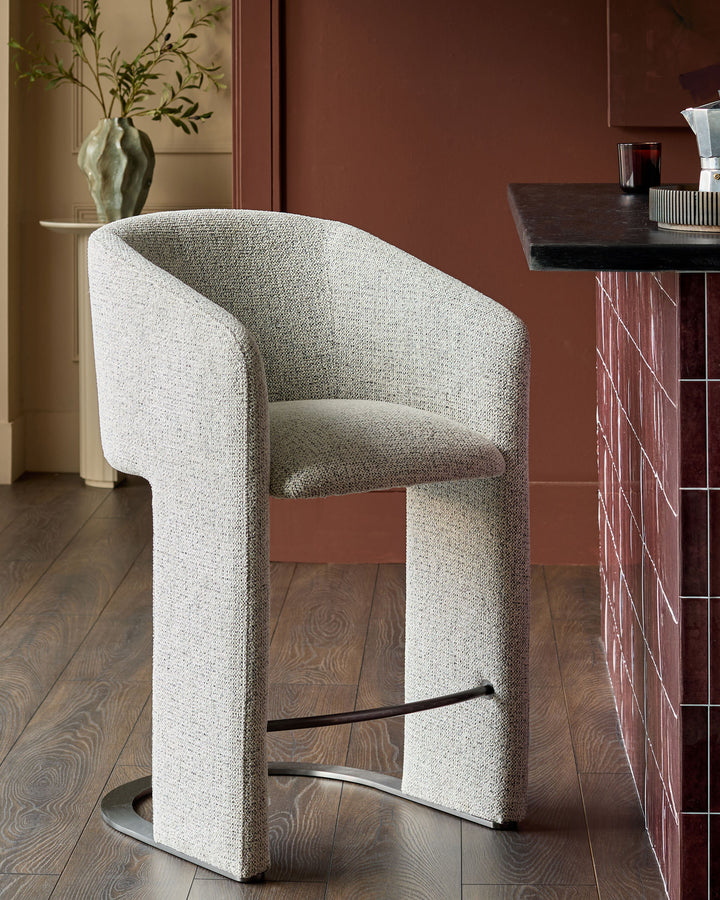 Leighton grey fabric bar stool with black steel cantilever base, shown in modern interior setting.