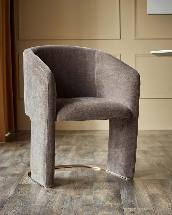 A modern brown velvet chair with a curved back and arms, on a light wooden floor.