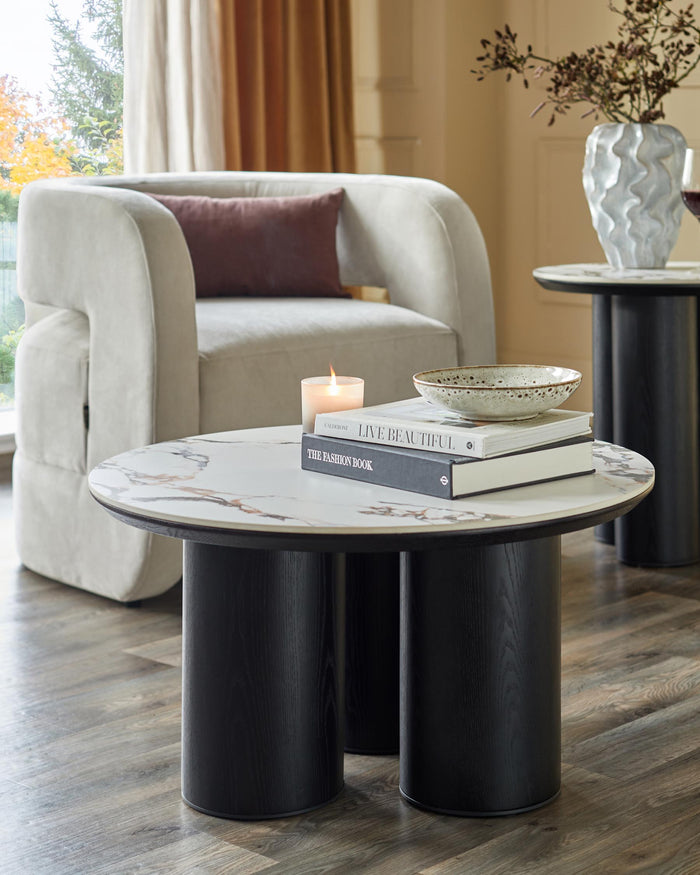 Stylish living room furniture: a round marble table, a sleek armchair, and a side table with a vase.