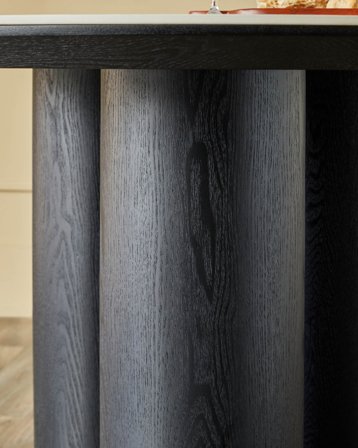 Close-up of a dark wooden table with cylindrical legs, showcasing the wood grain detail and modern design.