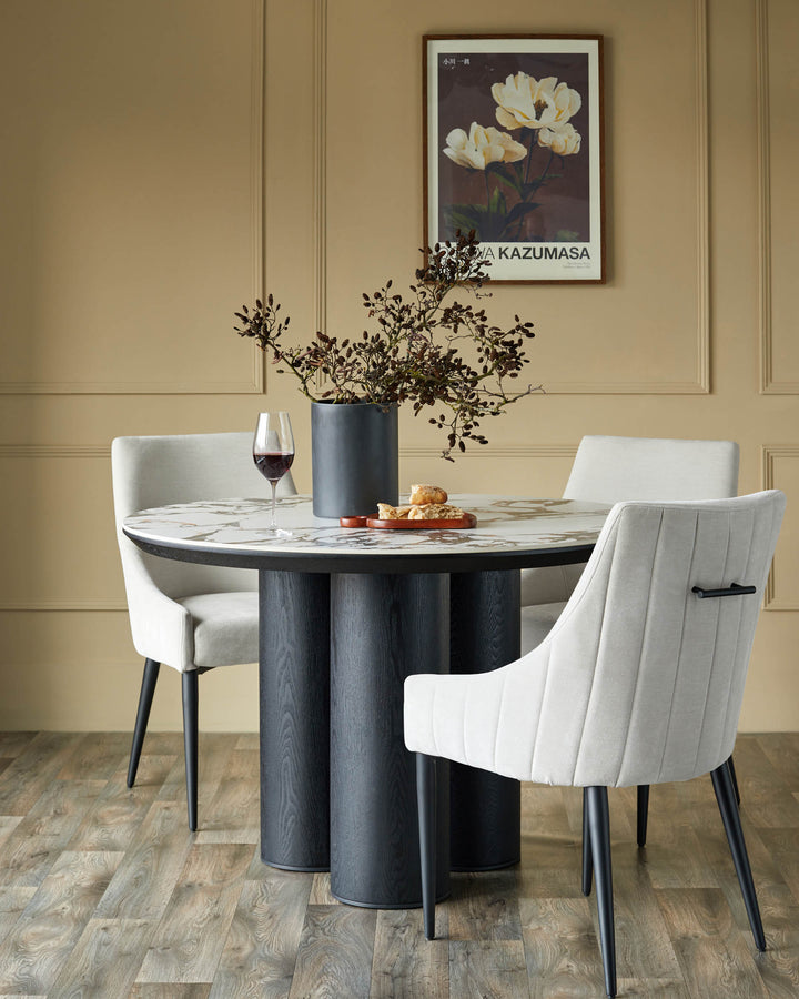 Stylish dining set featuring a round marble table, supported by a modern grey base, complemented by elegant upholstered chairs.
