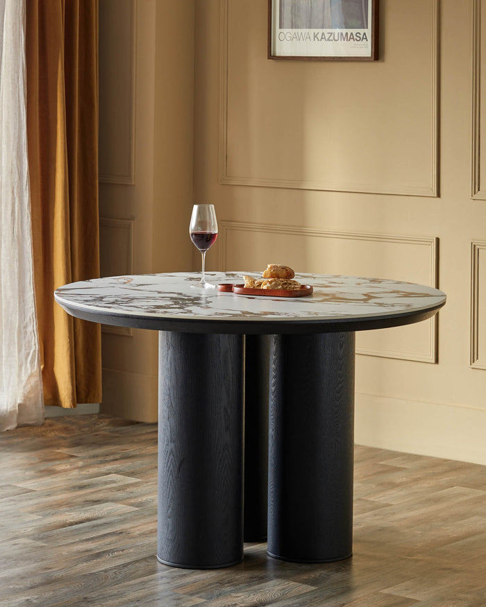 Round marble-topped dining table with cylindrical, dark wood legs. Wine glass and bread displayed on top.