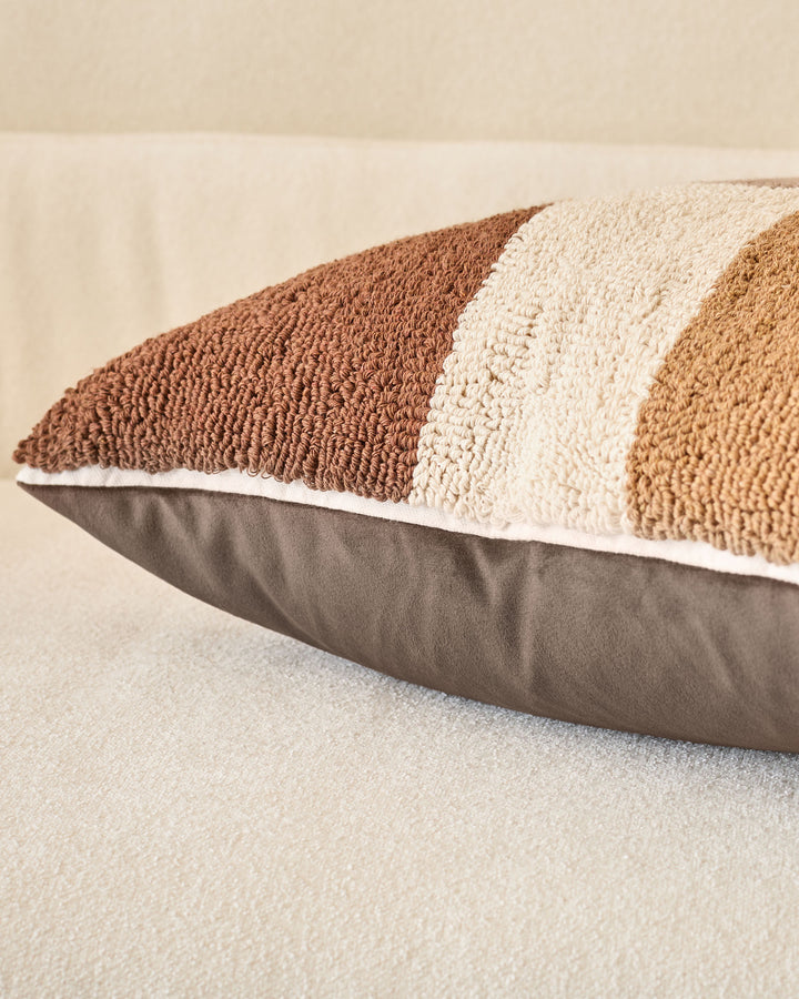 Lennon medium cushion in natural tones, showing striped textured fabric in brown, cream, and tan with gray base, angled view.