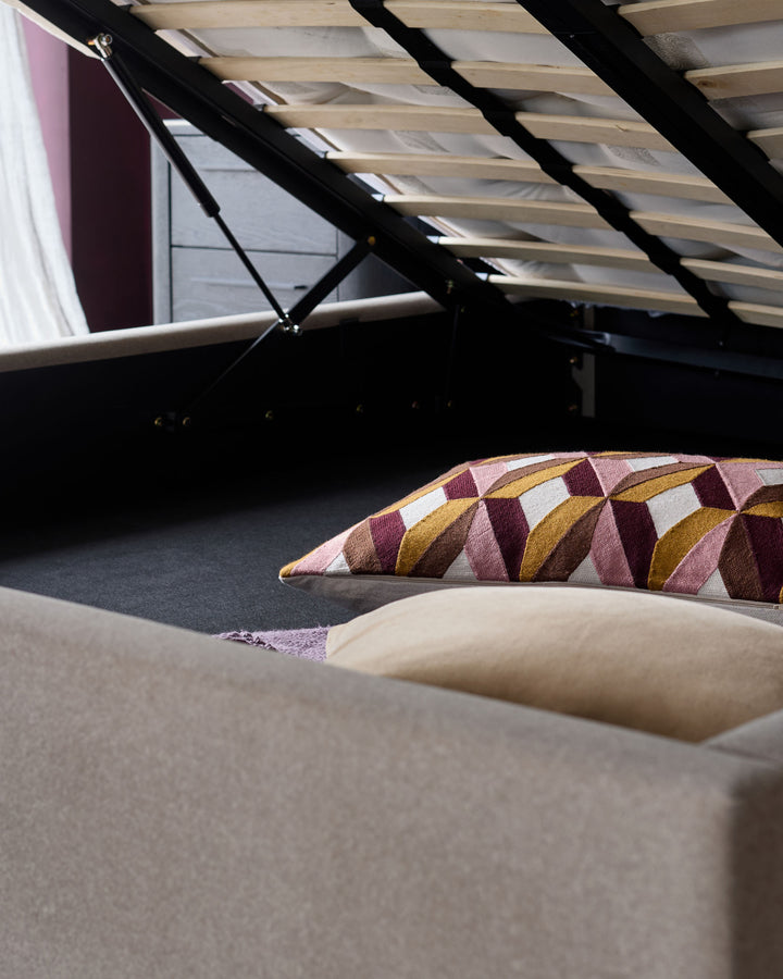 An open ottoman bed reveals storage space with a geometric pattern pillow and neutral tone cushions inside.