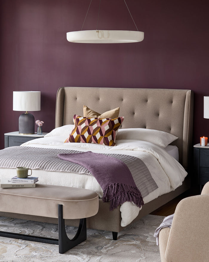 A bedroom with a large upholstered bed, bedside tables, a bench and accent chair, lit by an overhead light.