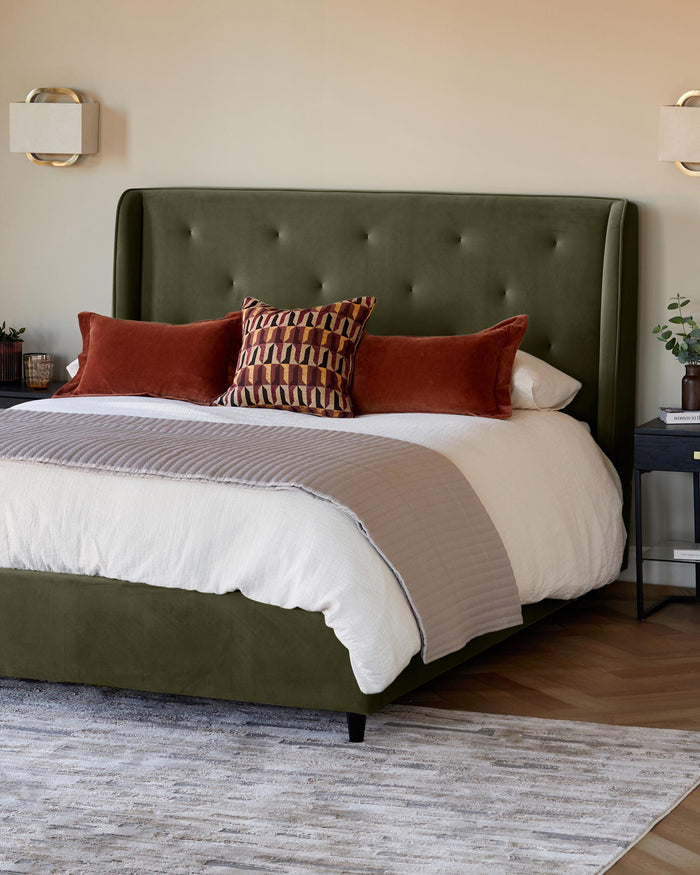 An olive green velvet bed with an upholstered headboard, featuring rust-coloured cushions, on top of a patterned rug.