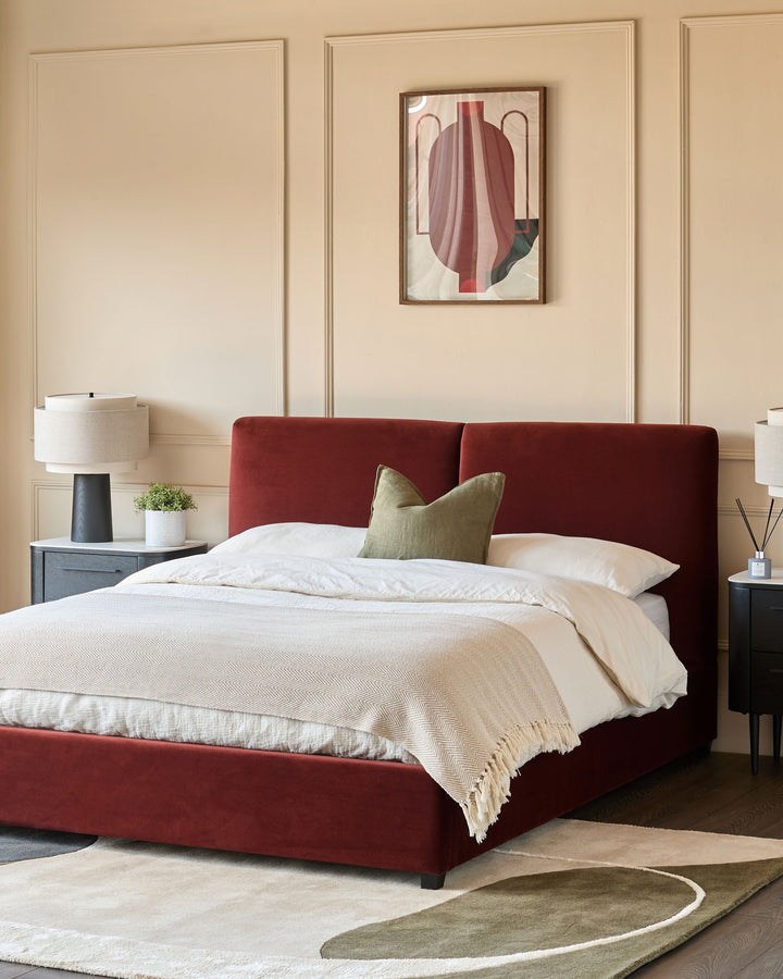 A double bed with a red frame, bedside tables with lamps, an abstract art print, on a cream & green rug.