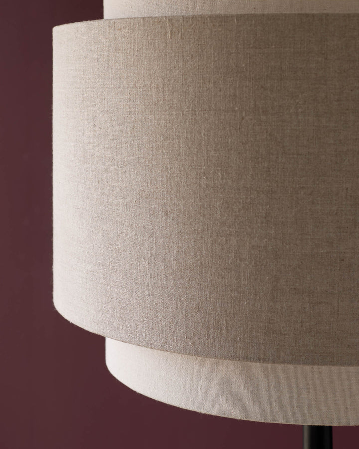 Leonie floor light with natural and mocha linen cylindrical shade, side angle view against burgundy background.