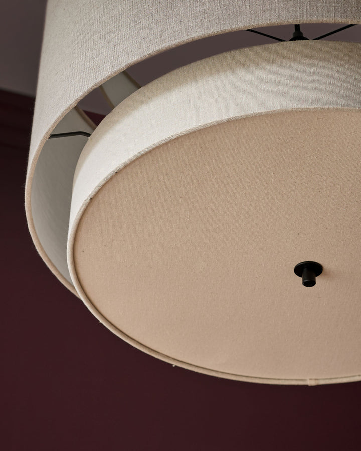 Layered linen pendant light with natural and mocha-colored fabric rings, shown from below against a burgundy background.