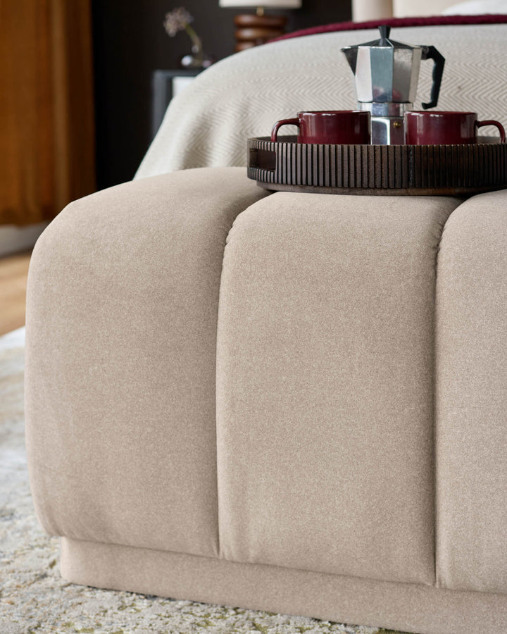 Cream fabric bench with curved, quilted sections and metal base, styled with coffee service on top.