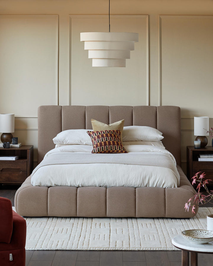 A stylish bedroom scene featuring a fabric-covered bed, matching bedside tables and a statement tiered pendant light.
