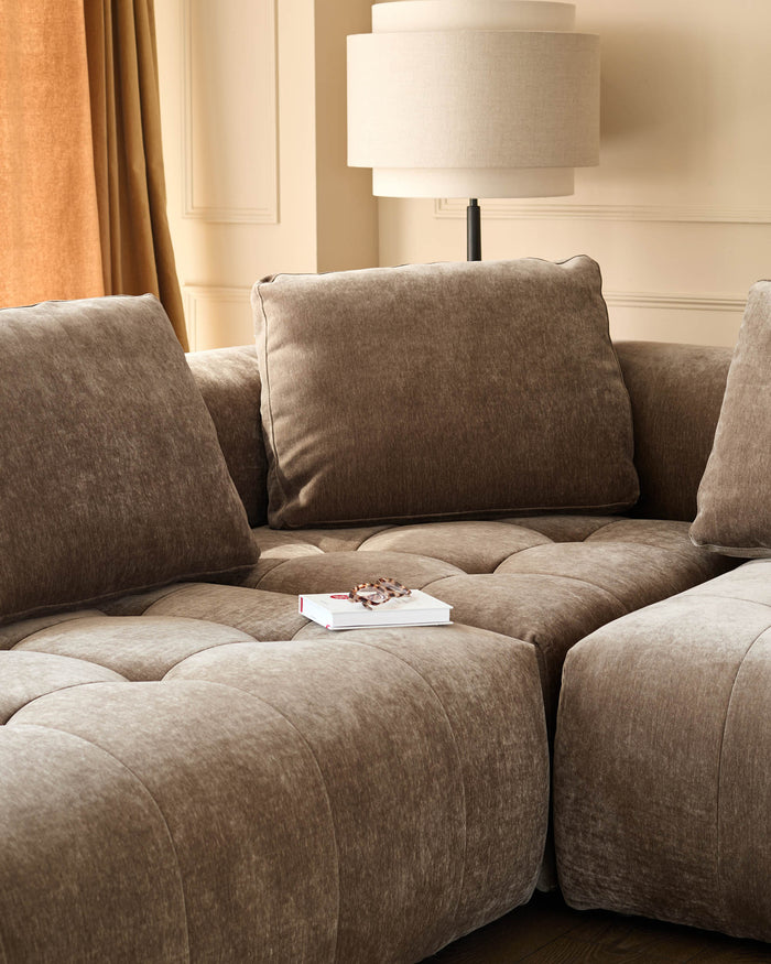 Close-up of a taupe modular sofa with large cushions and a book and glasses on top of one of the sections.