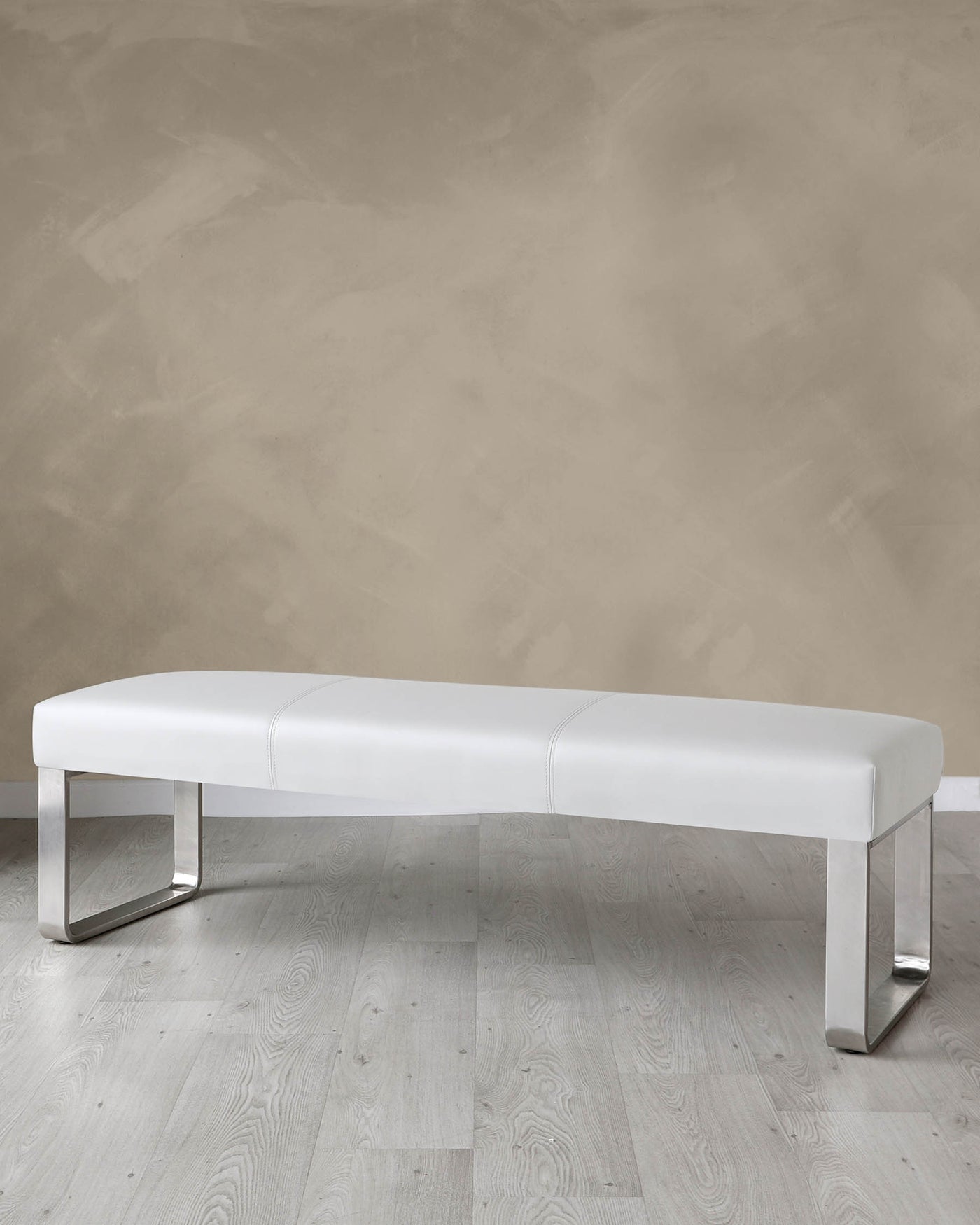 Modern white leather upholstered bench with sleek metallic legs set against a textured beige wall and light wooden flooring.