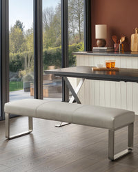 A modern grey bench seat with a metal frame sits on a wooden floor, complementing the table and minimalist interior.