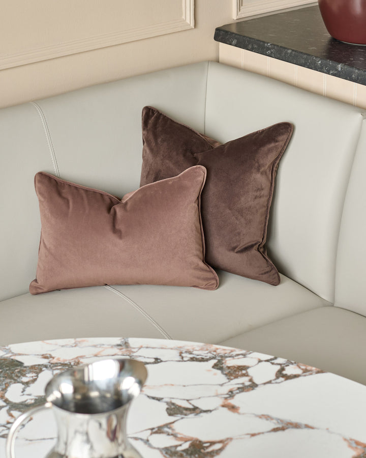 Light grey faux leather corner dining bench with brushed brass legs, styled with mauve velvet pillows and marble table.