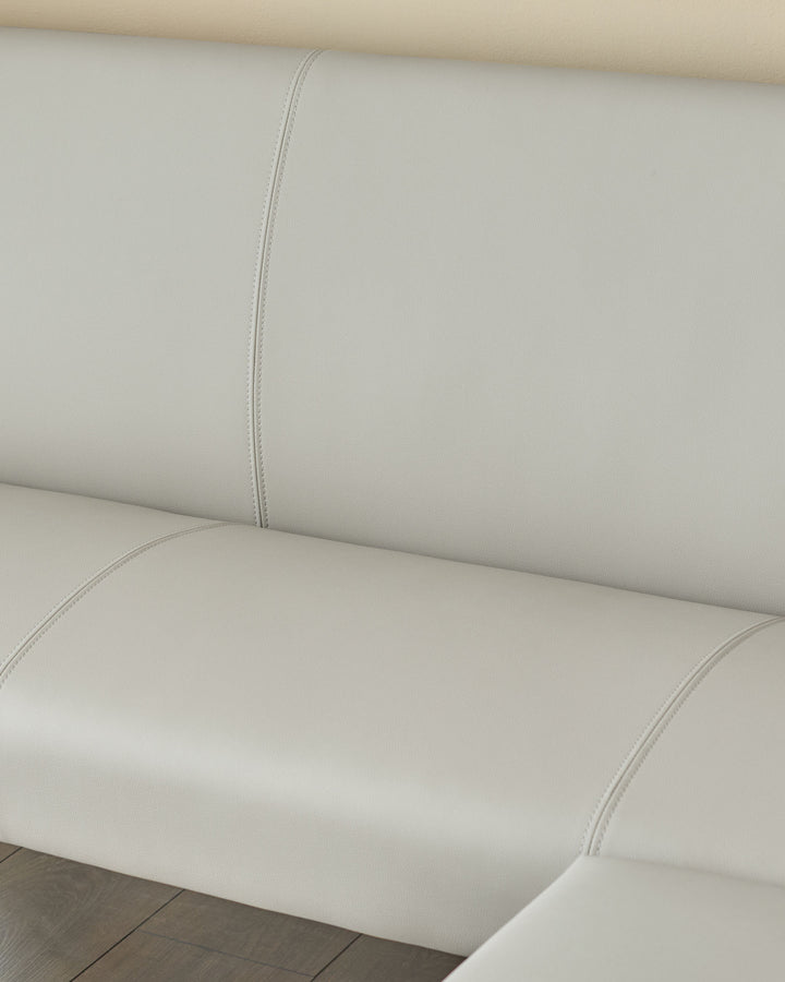 Light grey faux leather dining bench with stitched seams and chrome legs, angled view.