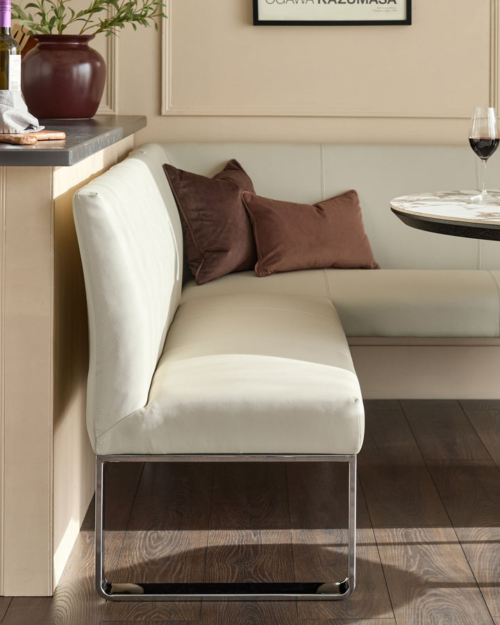 Light grey faux leather dining bench with chrome legs, styled with brown cushions in a contemporary dining room setting.