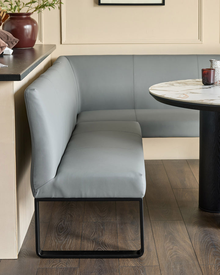 Grey upholstered corner bench with black metal legs, shown in a modern dining setting next to a round marble table.