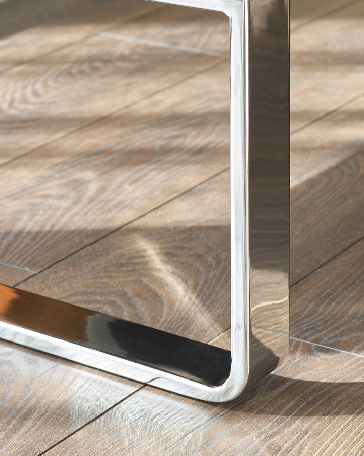 Close-up of chrome leg and white frame detail on grey faux-leather dining bench against wooden floor.