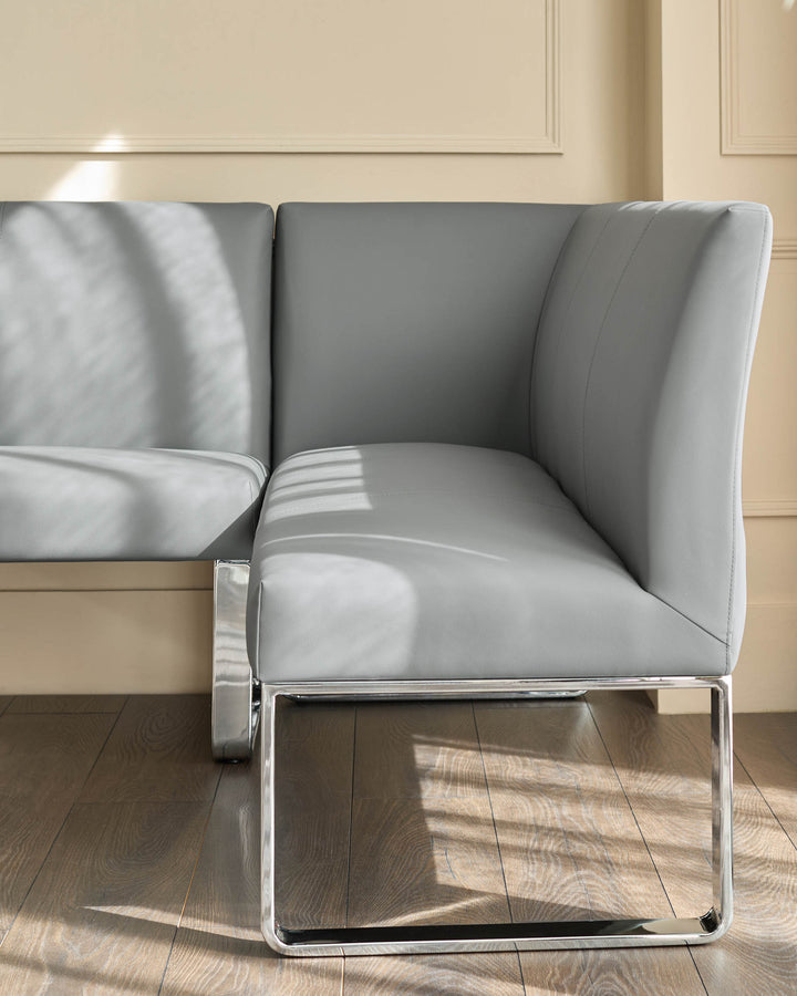 Grey faux leather corner dining bench with chrome legs, shown from side angle in modern room setting.