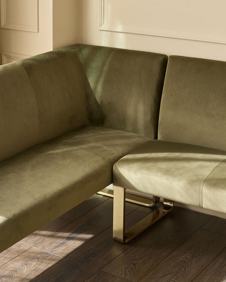 Olive green corner bench with brushed brass legs, angled view showing curved backrest and seating in minimalist interior.