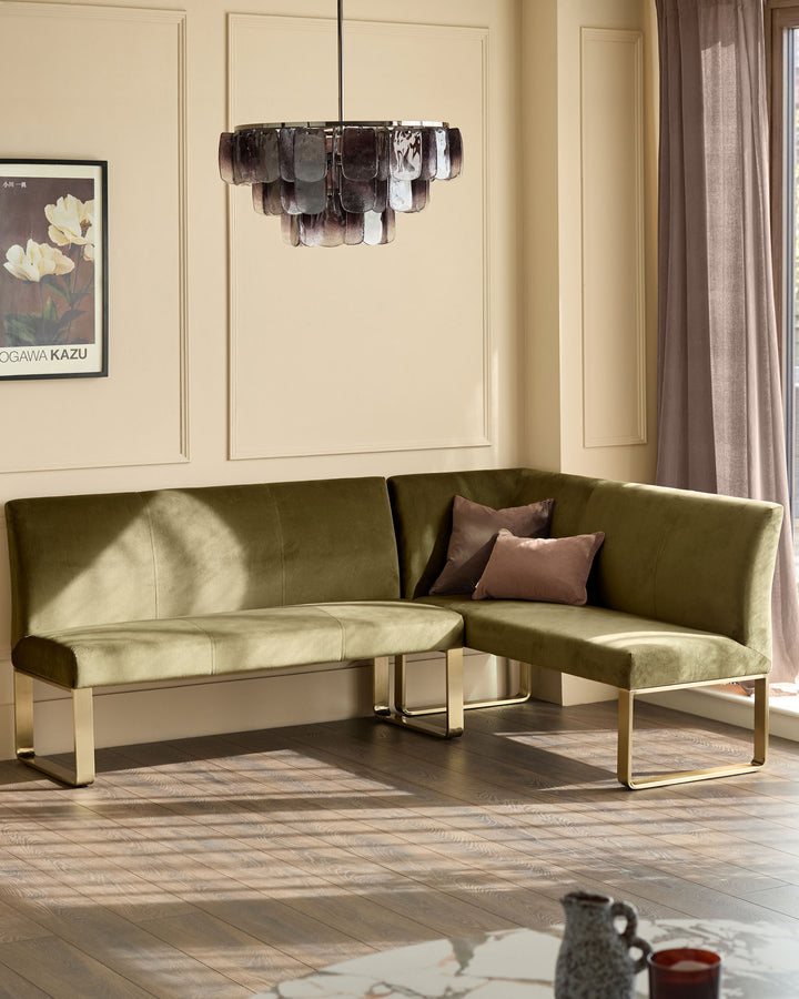 Olive green corner bench with brushed brass legs, styled in a modern living room with pendant light and cream walls.