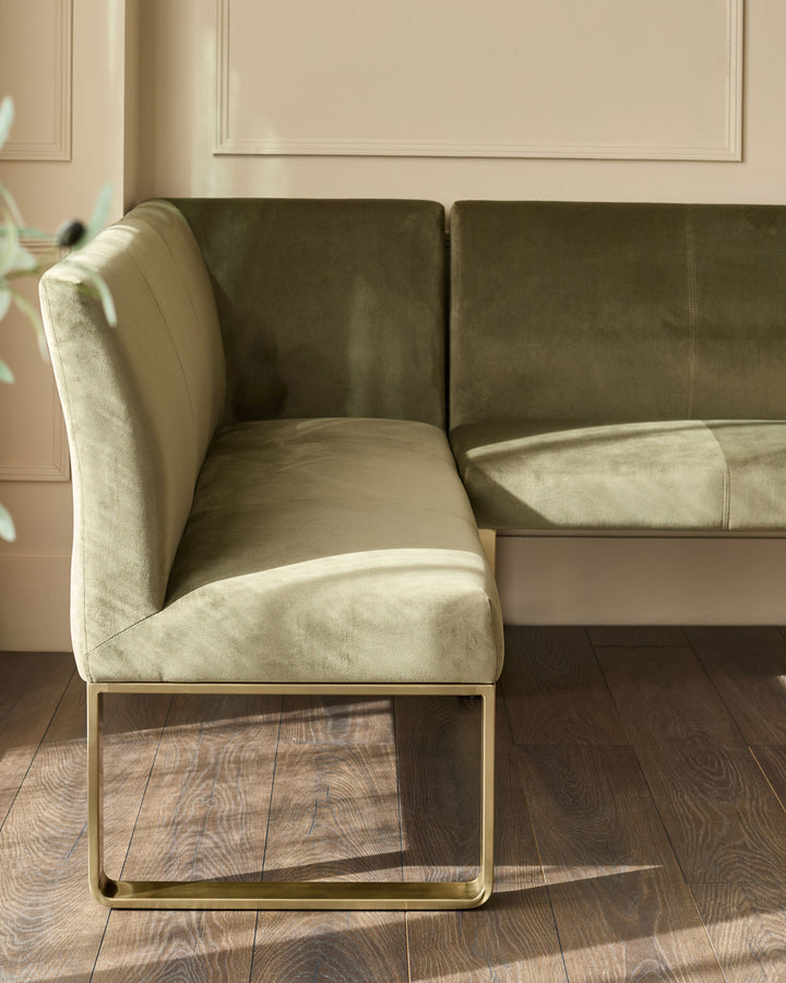 Olive green corner bench with brushed brass frame, shown from side angle in bright room setting.