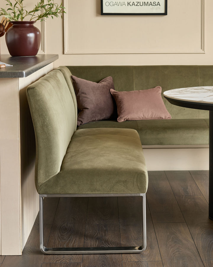 Olive green corner bench with stainless steel legs, styled with mauve pillows in a modern interior setting.