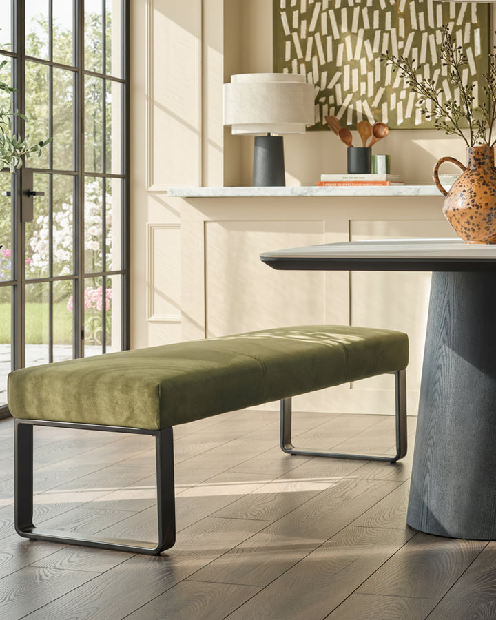 Loop 3-seater velvet bench without backrest, olive green upholstery with black metal frame, in contemporary room setting.
