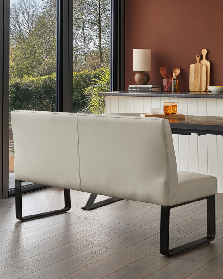 A contemporary, light grey bench seat with black metal legs positioned at a dining table next to a window in a modern home.