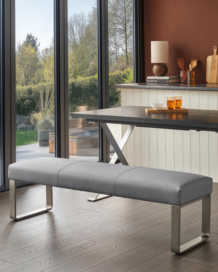 A grey bench sits by a table, illuminated by natural light pouring through large windows. Perfect for the modern dining room.