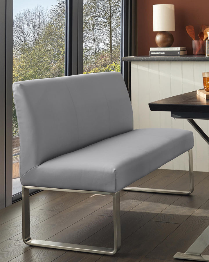 A modern grey bench with a sleek metal frame stands against a window, showcasing minimalist design and comfort.